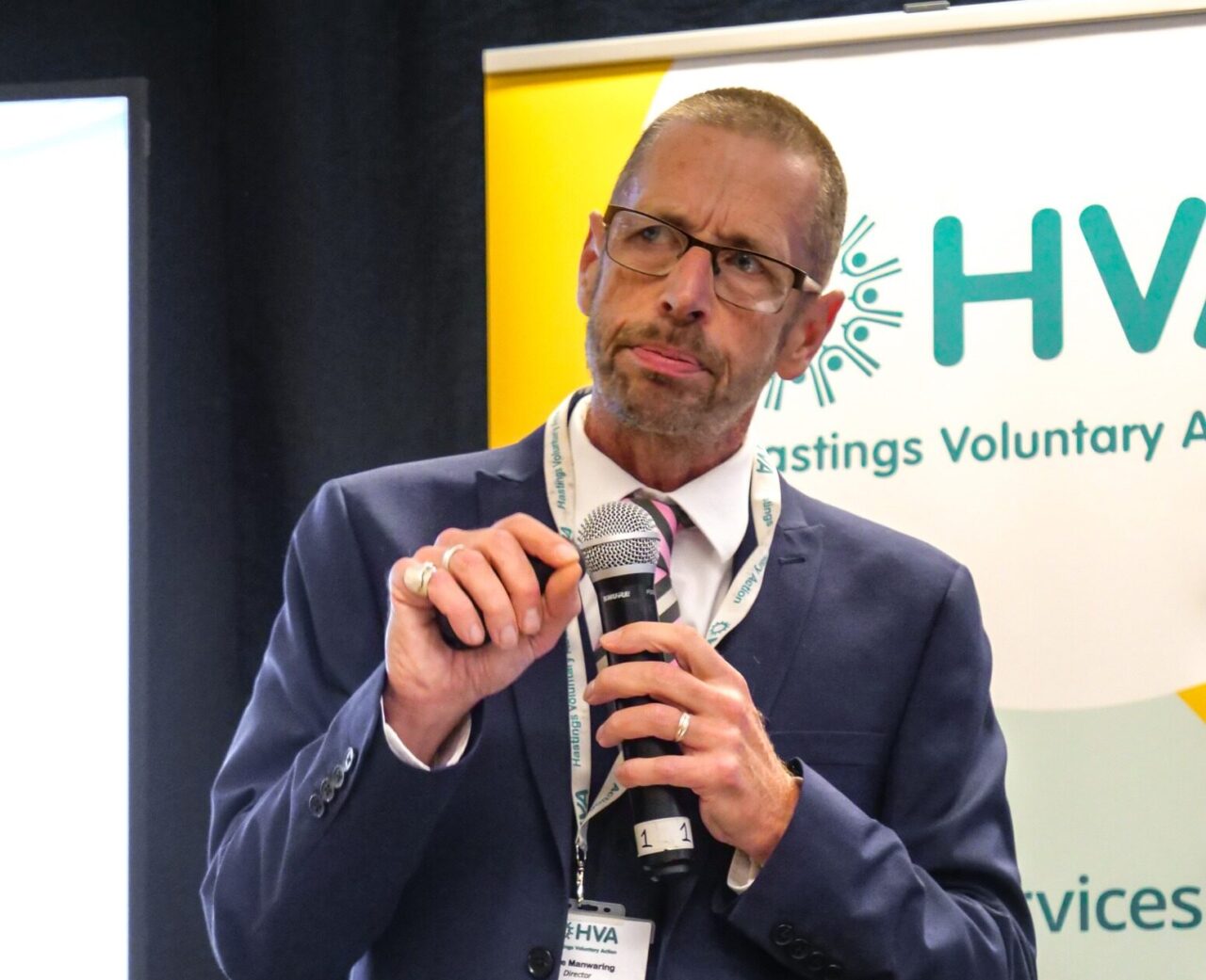 Steve Manwaring getting ready to give a speech. He is very smart in a blue suit and there is a big HVA poster behind him.